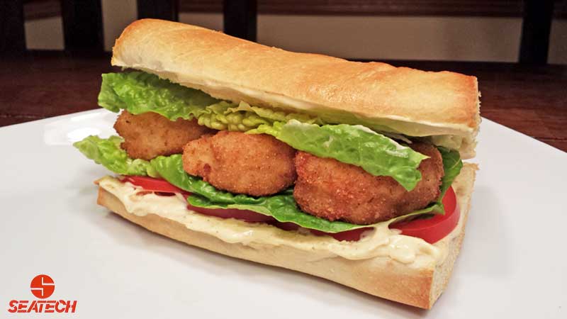 A photograph of an Argentine red shirmp poor boy on fresh french bread with lightly fried shrimp, lettuce, tomatoe mayo and mustard.