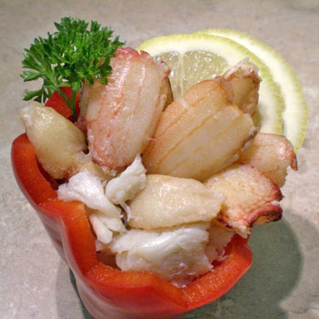 A photograph of handpicked Chilean crab meat placed inside a red bell pepper with a lemon wedge and parsley.