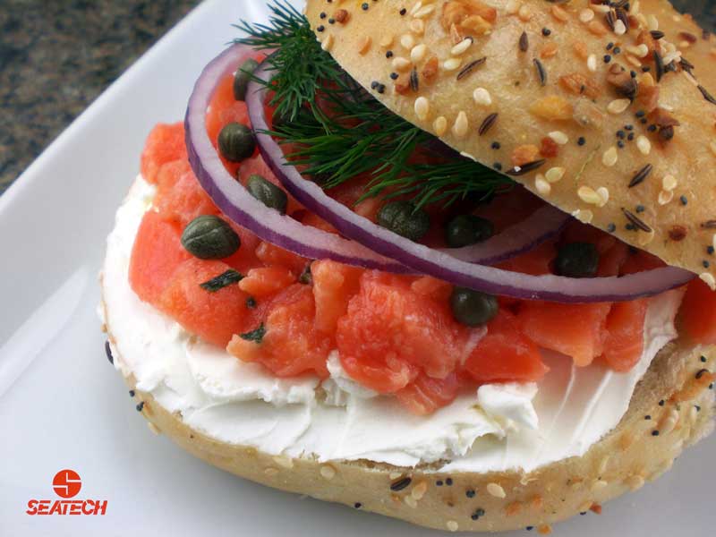 A photograph of a salmon tartar bagel with cream salmon tartar, cream cheese, red onions, capers and fresh dill on a bagel.