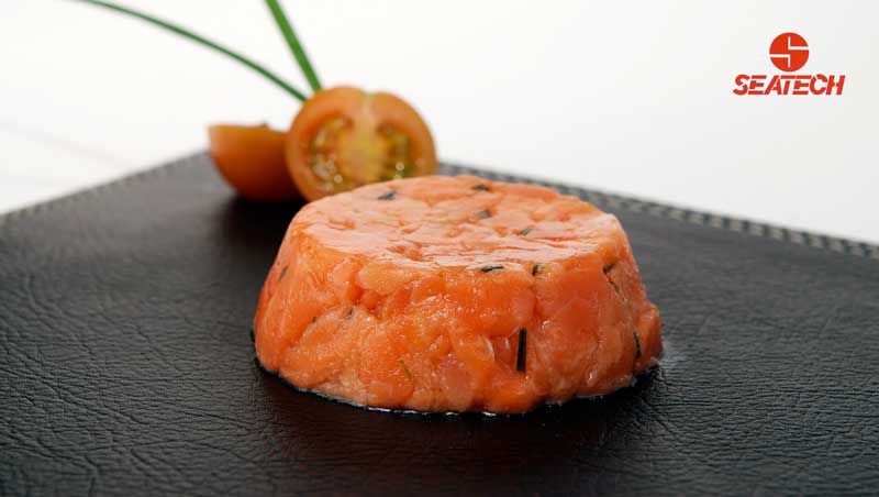 A photograph of salmon tartar with a sliced cherry tomato and chives.